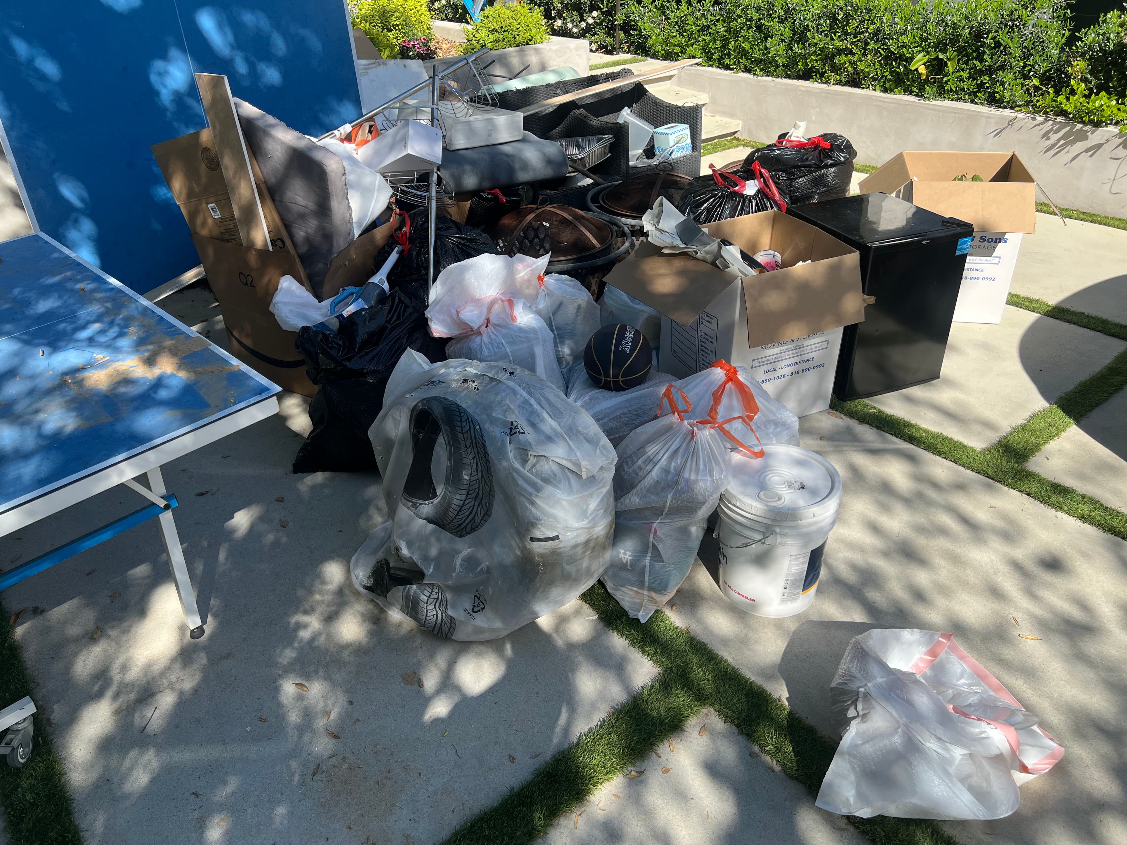 Cluttered outdoor space with trash bags, boxes, and discarded items on a patio.