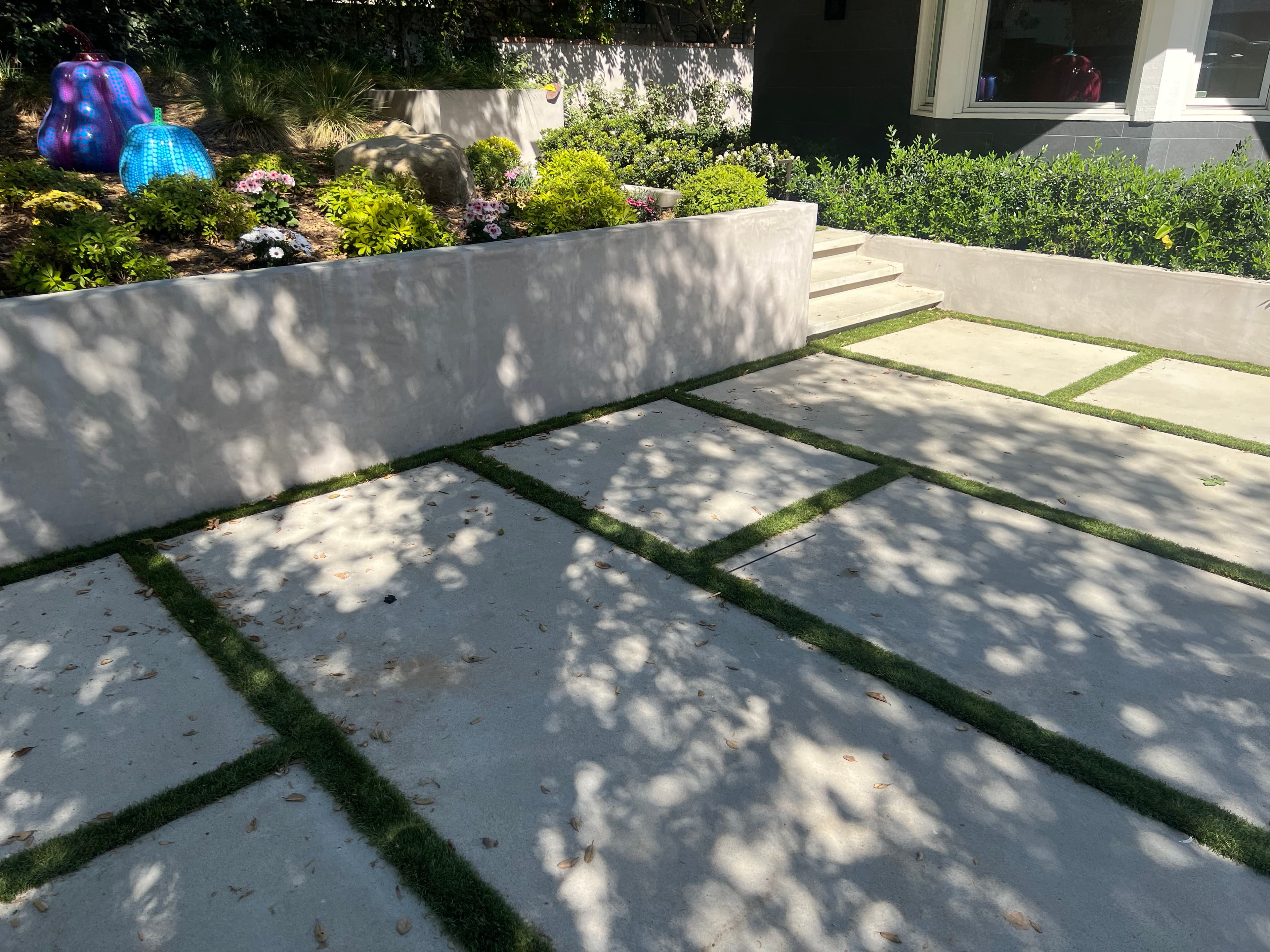 Modern outdoor patio with concrete slabs and grass patches, surrounded by vibrant landscaping.